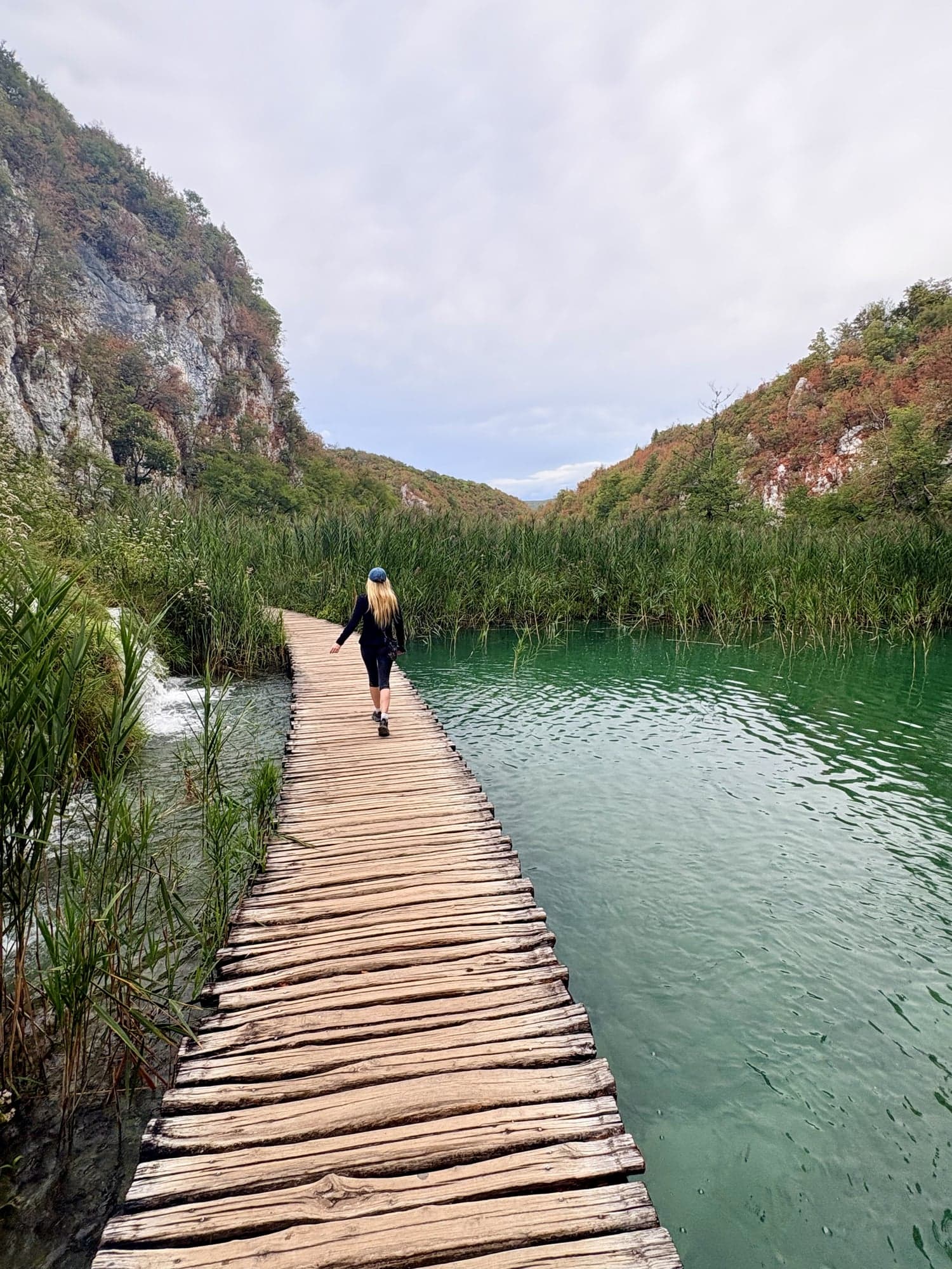 Hannah walking along a wooden boardwalk between turquoise water and reeds at Plitvice Lakes National Park